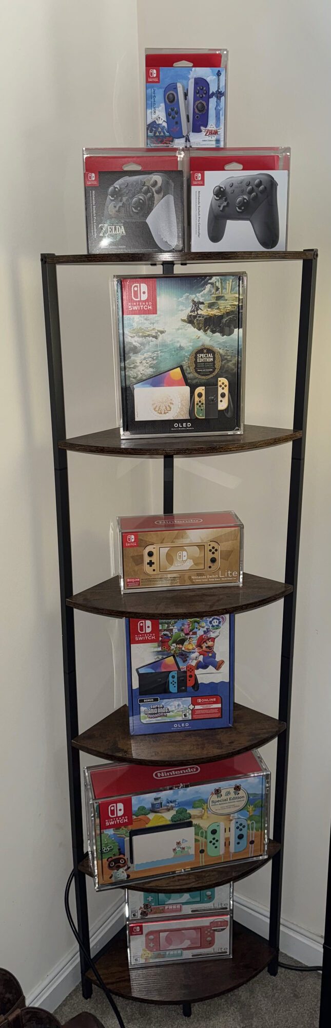 A corner shelf holding part of my Nintendo Switch collection, including OLED special editions, a Switch Lite, Pro controllers and Switch 2 consoles